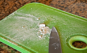 A crushed pill on a plastic Tupperware lid with a knife next to it