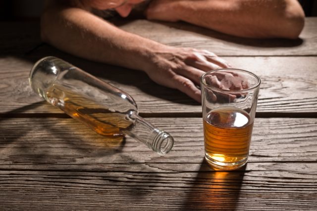 Passed out person next to bottle and a glass of alcohol