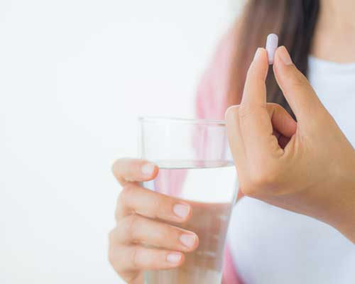 woman-holding-single-pill-and-glass-of-water-on-white-background