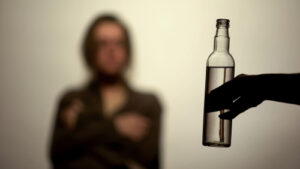 A bottle being held in front of a blurred out woman wearing a blanket