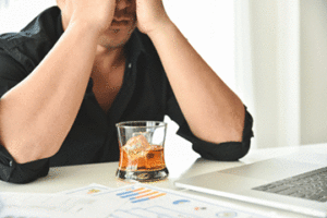 Stressed man with his hands on his face and a drink in front of him