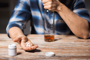 Man with an almost empty liquor bottle in one hand and several pills in the other