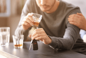 Man holding his car keys in one hand and a glass of whiskey in the other