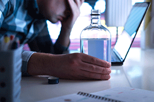 Man with a hand on his face in front of his laptop while drinking liquor