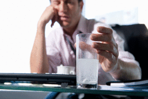 Sleepy man drinking alka-seltzer at work