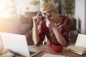 Stressed woman with glasses pinching her nose while working at her desk