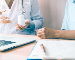 A doctor holding a pill bottle and speaking to a patient