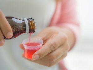 Woman pouring red cough syrup in a small plastic cup