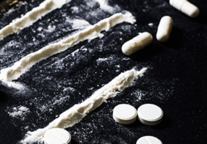 White pills, powder and tablets on a black table.