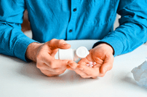 Person pouring pills into their hand from a white pill bottle in their other hand