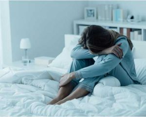 Sad woman with her head on her knees sitting on her bed