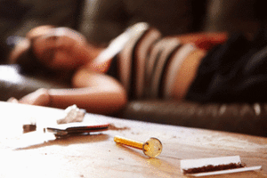 Person asleep on the couch with paraphernalia for meth use on a wooden table in front of her
