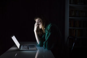 Stressed woman pinching her forehead in front of a laptop in a dark room
