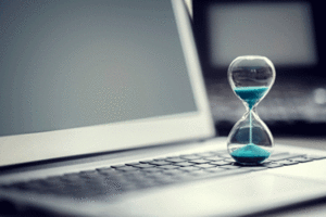 A small hourglass filled with blue sand on a laptop