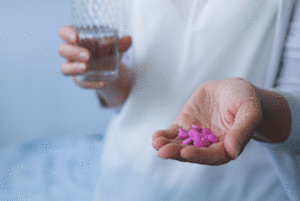 Woman holding pink pills in one hand and a glass of water in the other