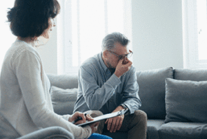 Man pinching his nose under his glasses sitting on a couch in a therapist's office