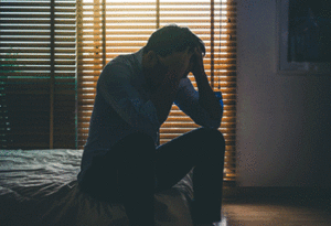 Sad man in a dim room with his hands on his head in frustration