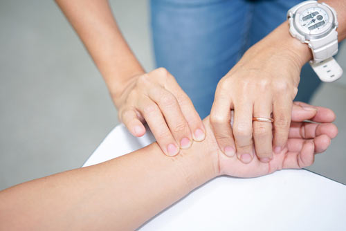 A nurse taking a patient's pulse on their wrist.