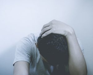 A young boy with his head down and his hand on his head.