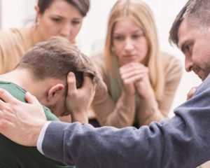 A circle of people consoling a man with his head down