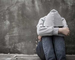 Sad young man in a hoodie with his head in his knees