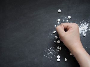 A fist crushing white pills against a black surface